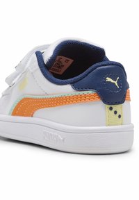 Baskets blanches avec des accents marine, des rayures orange et vert clair, et des bandes Velcro. Semelle en caoutchouc texturée et détail du logo sur le talon.