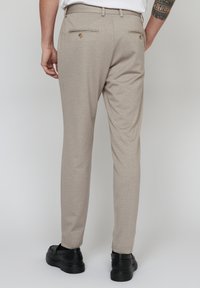 Pantaloni personalizați de culoare bej deschis, cu o textură subtilă, având două buzunare la spate cu butoane rotunde și un design slim fit. Pantofii negri completează ținuta.