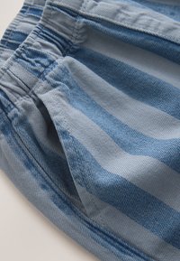 Primer plano de tela vaquera a rayas azules con una cinturilla elástica fruncida y un bolsillo lateral.