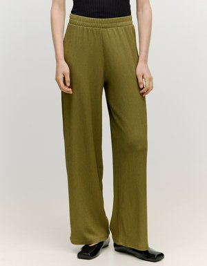 Olijfgroene wijde broek met een gestructureerde afwerking, elastische tailleband en een losse pasvorm, gecombineerd met zwarte platte schoenen.