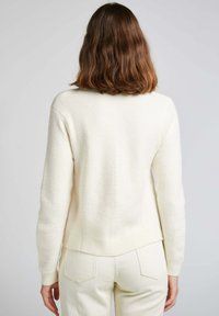 Pull en tricot couleur crème avec texture côtelée, longueur légèrement raccourcie, col rond et manches longues. Présente un détail de couture lisse dans le dos.