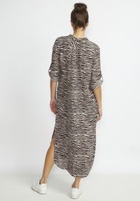 Lång, lös passande klänning i beige med ett svart zebramönster. Har uppvikt ärm och sidofickor, tillverkad av lättviktig tyg.