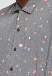 Camicia grigia a maniche corte con un motivo di forme rosa, blu e bianche sparse, dotata di colletto classico e bottoni neri.