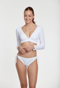 White long-sleeve bikini top with a v-neckline and twist detail, paired with white bikini bottoms featuring tie sides. Smooth, ribbed texture.