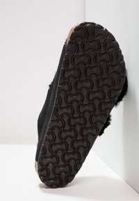 Chinelo preto com sola de borracha texturizada, apresentando uma textura de pelo suave na parte superior e um design arredondado para conforto.
