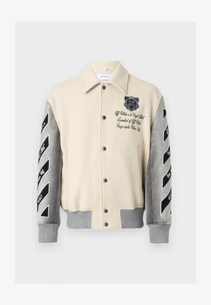 Veste universitaire beige et grise avec des rayures diagonales noires sur les manches et du texte brodé sur la poitrine et les bras, fermeture avant à boutons.