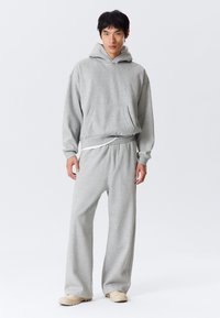 Grå bomulds-sweatshirt med hætte, kængurulomme og ribbet kant, kombineret med matchende vidde-sweatpants og beige slip-on sko.