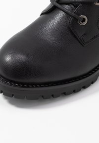 Botte en cuir noir avec une finition texturée, dotée de lacets ronds, d'œillets en métal et d'une semelle extérieure épaisse et robuste pour une meilleure traction.