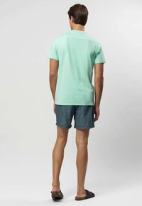 Krótka koszulka w miętowym zielonym kolorze, wykonana z bawełny; w połączeniu z granatowo-białymi szortami w paski, projekt płaski, oraz brązowe sandały na wsuwanie.