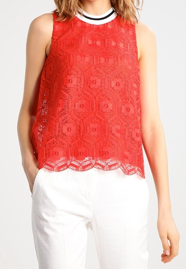 Débardeur en dentelle rouge avec un motif floral, un ourlet festonné et un col rond rayé noir et blanc, associé à un pantalon blanc texturé.
