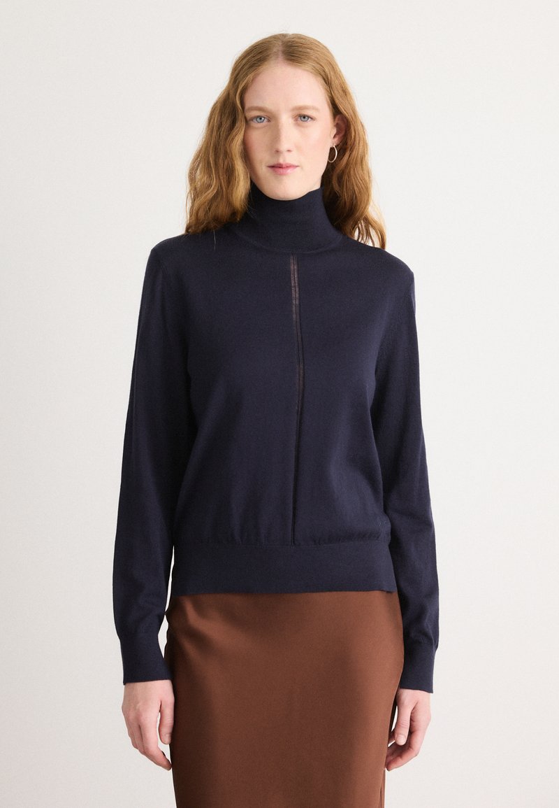 Marineblå turtleneck genser med halvglidelås foran, lange ermer og tettsittende kant. Myk tekstur, laget av et lett strikkemateriale.