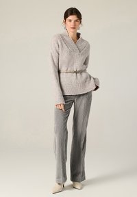 Maglione grigio chiaro con texture e colletto a scialle, abbinato a una cintura sottile beige, pantaloni a gamba larga grigi con righe e tacchi beige.