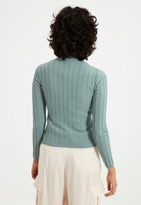 Jasnozielona prążkowana bluzka z długimi rękawami i wysokim dekoltem. Charakteryzuje się dopasowanym krojem oraz teksturowanym materiałem dla dodatkowego efektu.