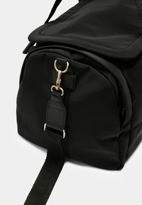Sac en nylon noir au design rembourré, doté d'un fermoir en métal doré et d'une bandoulière à motif. Texture lisse et quincaillerie solide.
