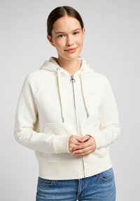 Weiße Kapuzenjacke mit Reißverschluss, Kordelzugkapuze, Kängurutaschen und gerippten Bündchen. Glatte Stoffoberfläche mit dezentem Logo-Detail auf der Brust.