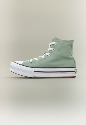 Wysokie trampki wykonane z jasnozielonego płótna, z białymi sznurowadłami, gumowym noskiem i grubą białą podeszwą z czarnymi paskami.