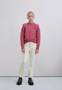 Suéter de punto texturizado rosa con detalles en los hombros, combinado con jeans acampanados de tiro alto blancos y botas gruesas negras.