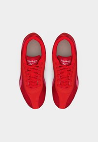 Ζευγάρι κόκκινα sneakers Reebok με κορδόνια, που φαίνονται από πάνω σε απλό λευκό φόντο.