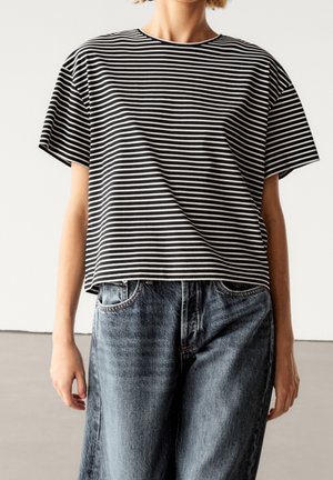T-shirt à manches courtes à rayures noires et blanches avec une coupe ample, associé à un jean en denim bleu délavé taille haute. Encolure ronde simple.