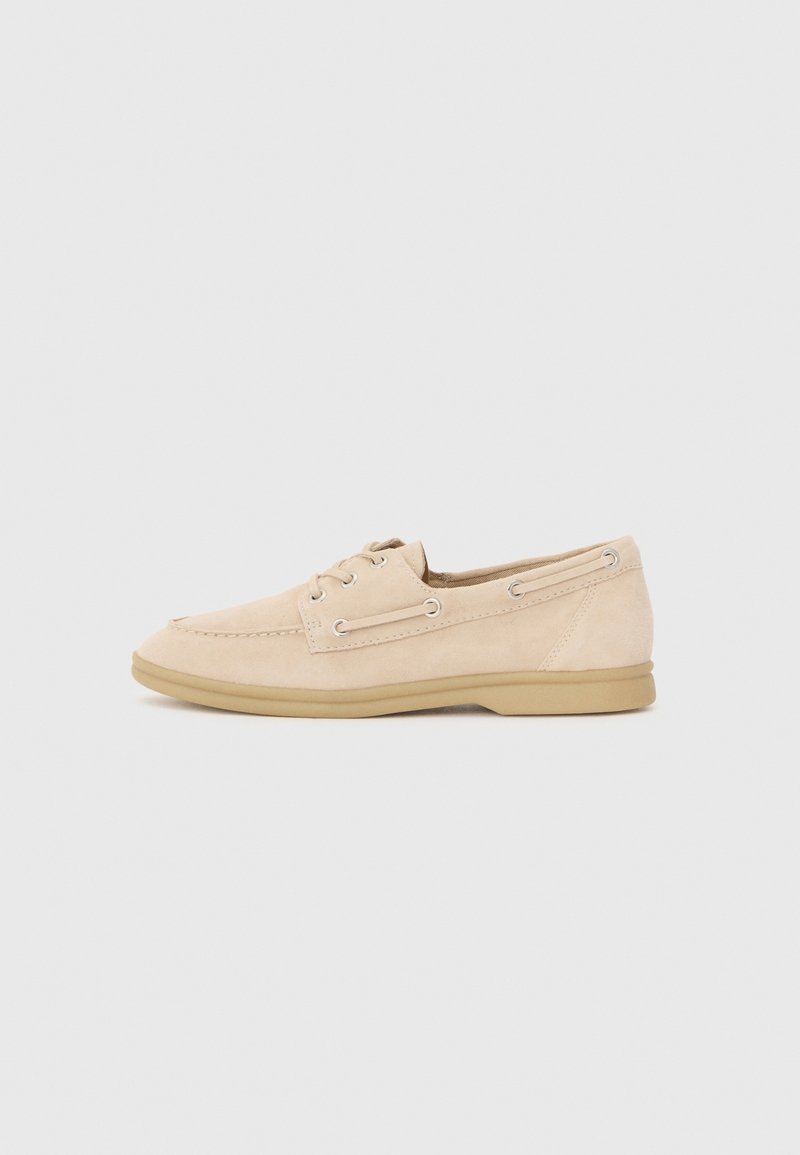 Chaussure bateau beige en daim décontractée à lacets avec couture moc toe et semelle en caoutchouc marron clair, vue de profil sur fond uni.