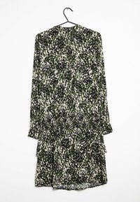 Vihreä ja musta kuviollinen pitkähihaine mekko, jossa on rypytetty vyötärö ja kerrokselliset hameet, roikkumassa mustassa koukussa valkoista taustaa vasten.