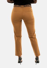 Bruine slim-fit broek met achterzakken en een textured di print tailleband. Gedragen met zwarte hoge hakken, recht gesneden ontwerp.