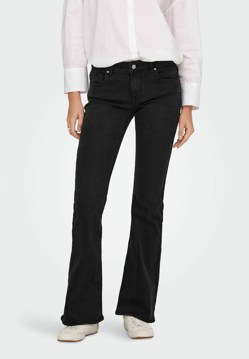 Sorte flared jeans lavet af denim, med en tætsiddende talje og lige ben. Båret med en hvid skjorte med knapper og hvide sko.