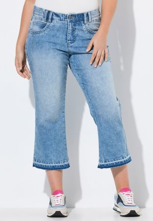 Jeans courts bleu clair à jambe large, dotés de passants de ceinture, de poches avant et d'un ourlet effiloché. Associés à des baskets blanches et grises.