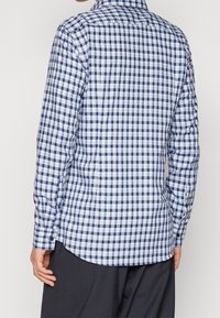 Camicia a maniche lunghe a quadretti blu e bianchi con polsini abbottonati, fondo arrotondato e dettaglio sulla spalla posteriore. Tessuto di cotone con una consistenza liscia.