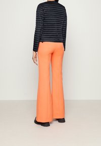 Black puffer jacket with a quilted pattern, paired with bright orange flared pants, featuring a smooth texture and visible stitching details.