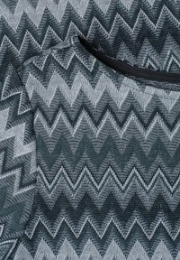 Tissu à motif zigzag gris foncé et gris clair avec une texture tissée et une petite ouverture au col bordée de noir visible.
