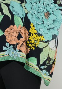 Blusa floreale con grandi peonie turchesi, rose arancioni e fiori gialli su sfondo nero. Orlo testurizzato con accenti a righe colorate.
