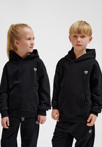 Svarta hoodies gjorda av mjukt material, med stora huvor, framfickor och små logotypdetaljer på bröstet. Enkla, avslappnade passform.