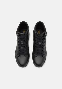 Paire de baskets montantes en cuir noir avec lacets et fermetures éclair latérales, vues de dessus sur fond blanc.