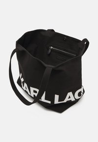 Czarna torba na ramię z białym logo "KARL LAGERFELD", wykonana z materiału tekstylnego, z wydłużonymi ramiami i wewnętrzną kieszenią na zamek.