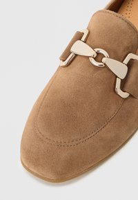 Ταμπά μοκασίνια από σουέτ με λεία υφή, τετράγωνη μύτη και ένα μεγάλο διακοσμητικό αλυσίδα σε χρυσό τόνο στο πάνω μέρος.