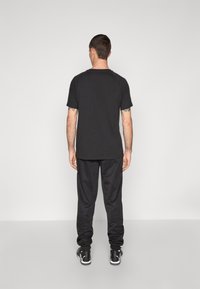 Sort kortærmet t-shirt med rund hals, parret med sorte sweatpants. Stoffet ser glat ud, med en afslappet pasform og ingen synlige mønstre.