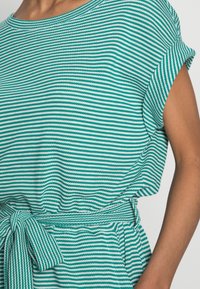 Vihreä ja valkoinen raidallinen paita lyhyillä hihoilla, pyöreällä kaula-aukolla ja sidotulla vyötäröyksityiskohdalla. Valmistettu teksturoidusta kankaasta.