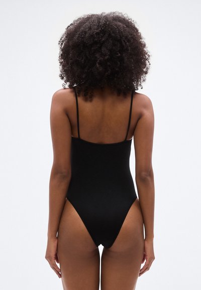 Maillot de bain une-pièce noir avec bretelles fines et dos échancré. Texture lisse et coupe ajustée mettant en valeur les contours du corps.