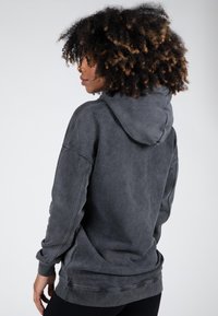 Donkergrijze hoodie met een zachte textuur, oversized ontwerp en een trekkoordcapuchon. Voorzien van ribgebreide manchetten en onderrand met een vervaagde, vintage uitstraling.