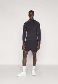 Fekete hosszú ujjú sportpóló raglán ujjakkal, fekete rövidnadrággal párosítva. A szettet fehér tornacipő és boka zokni egészíti ki.