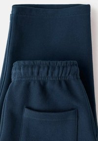 Námornícke modré tepláky vyrobené z mäkkého materiálu, s elastickým pásom a zadnou vreckom. Hladká textúra s jednoduchým dizajnom.