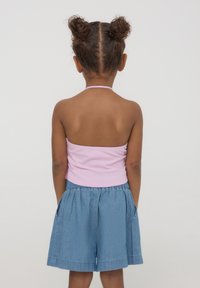 Top rosa con collo all'americana e un design aderente, abbinato a pantaloni shorts in denim blu larghi con tasche laterali e una cintura elastica.