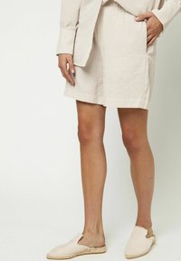 Pantalones cortos a rayas beige y blancos con corte recto, que cuentan con bolsillos laterales y un tejido texturizado. Combinados con zapatos tipo slip-on en beige claro.