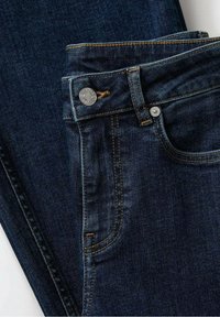 Jeans de denim azul oscuro con una textura suave, que presentan costuras de cobre, un cierre de botón plateado y un contorno de bolsillo delantero.