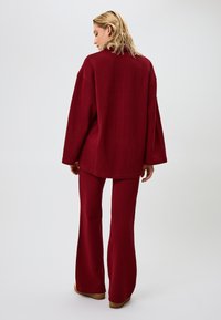 Bordeaux loungewear set met een losse top met verlaagde schouders en flared broeken van een gestructureerde gebreide stof. Glad zichtbare naden.