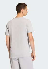 Svetlošedé tričko s krátkym rukávom z textúrovaného materiálu, s okrúhlym výstrihom a voľným strihom, nosené s tmavosivými šortkami rovnakej farby.