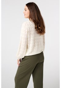 Pull crème en tricot avec motif en cœur, présentant des manches ballons et une coupe décontractée. Associé à un pantalon tailleur vert olive.