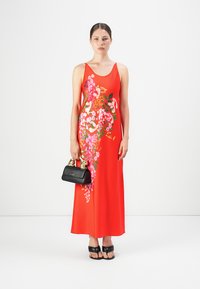 Vestido maxi floral rojo con un diseño sin mangas. Presenta un vibrante patrón floral en tonos de rosa y verde. Combinado con un bolso negro.