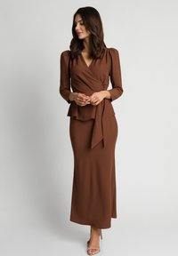 Brązowa sukienka rozkloszowana z długimi rękawami i peplum w talii. Wykonana z gładkiego materiału, ma głęboki dekolt w kształcie litery V i wiązanie w talii.